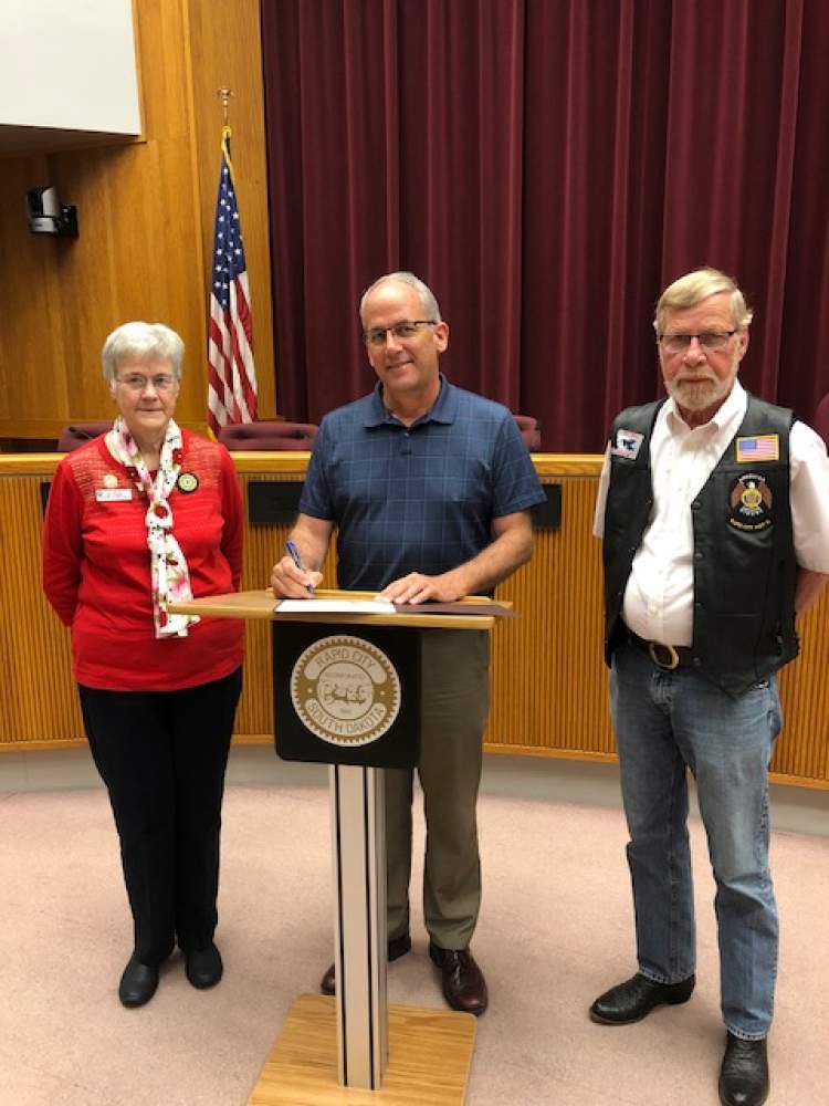 Mayor Steve Allender signs a mayoral proclamation declaring May 25 as National Poppy Day in Rapid City.  He is joined by American Legion Auxiliary State Poppy Chairwoman Sue Frantzick and her husband Leon.