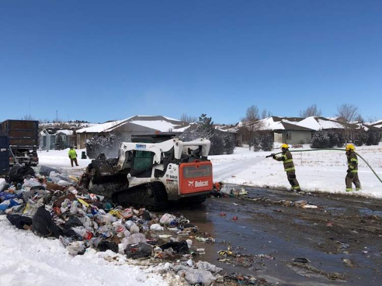 Solid Waste and Rapid City Fire Department crews work to scatter, douse and collect trash materials on Minnesota Street. A Solid Waste collection driver was forced to dump contents on the street after items within the garbage truck ignited.